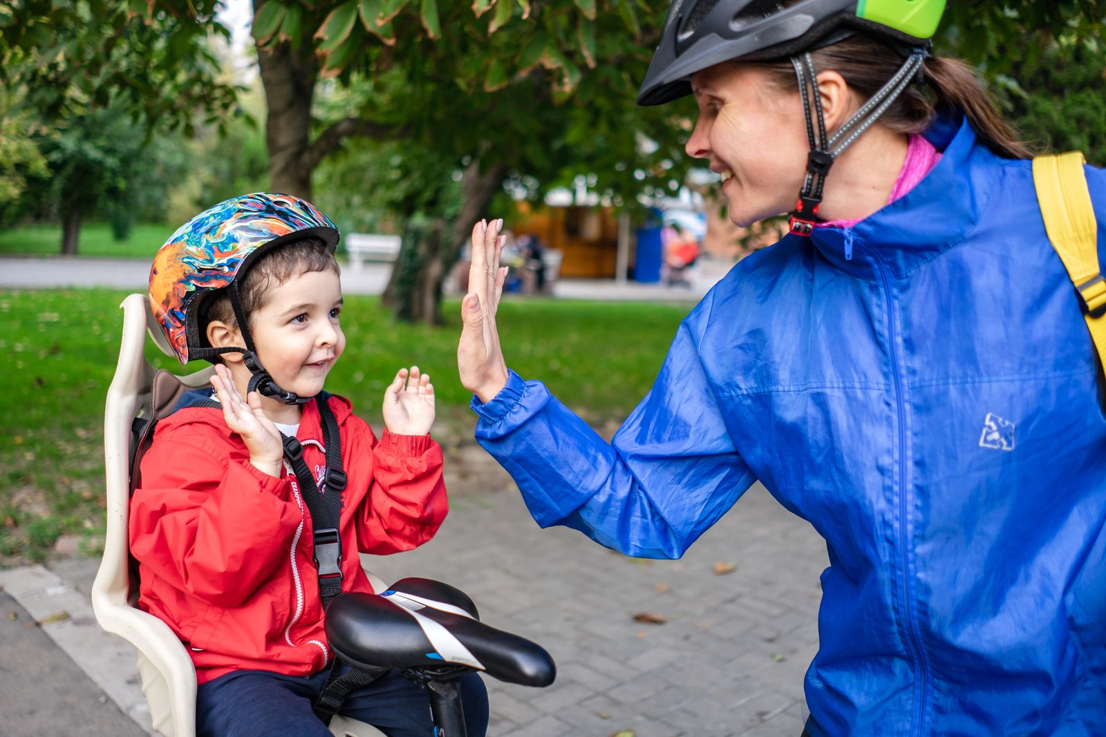Mutter und Kind geben sich lachend ein High-Five, beide mit Fahrradhelm